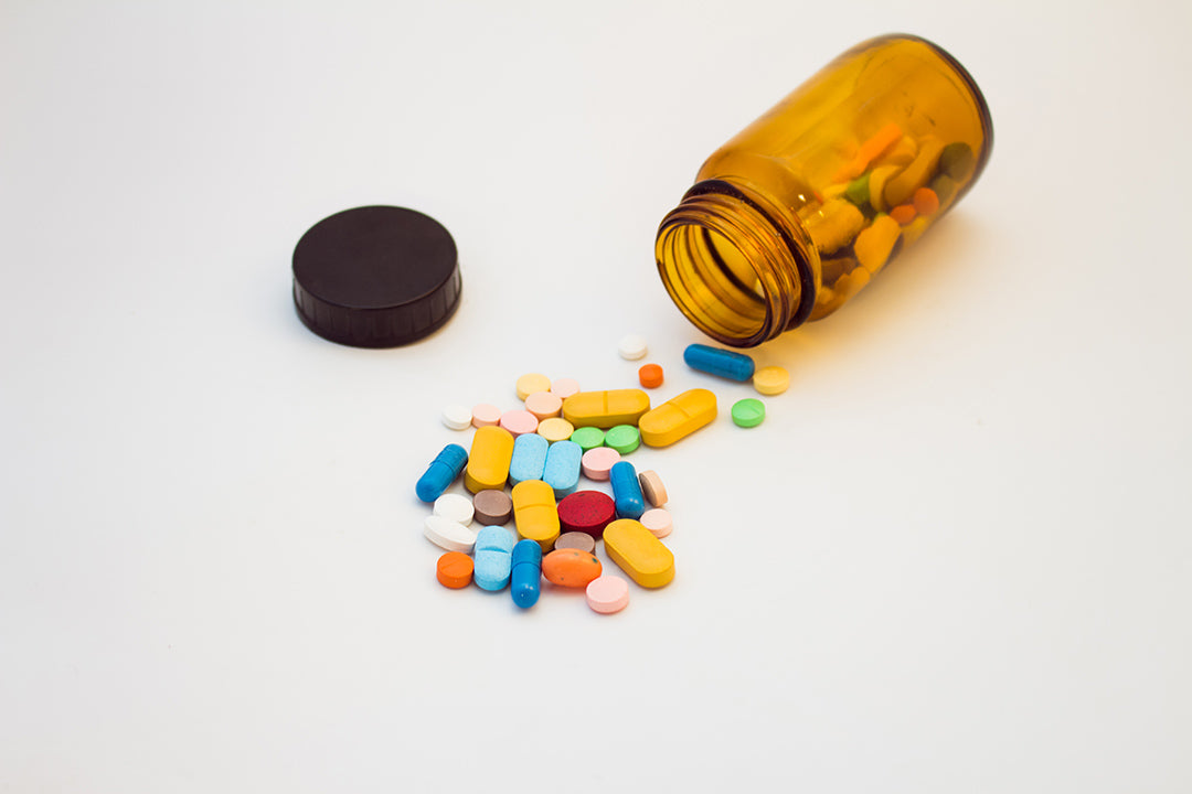 Nutraceutical tablet and capsule manufacturing at Biowell Labs—various colorful supplements spilled from an amber pill bottle onto a white background, showcasing high-quality contract supplement manufacturing and private label supplements production.