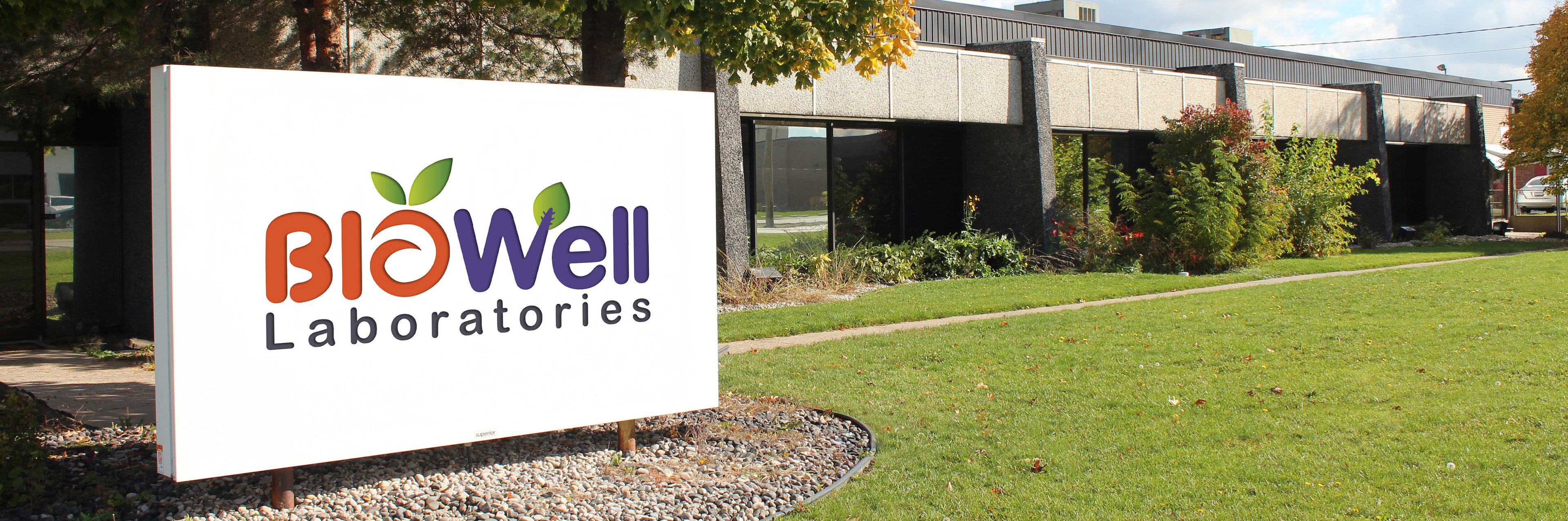 Biowell Laboratories facility exterior with company signage on a bright green lawn, showcasing a modern nutraceutical manufacturing and research center.