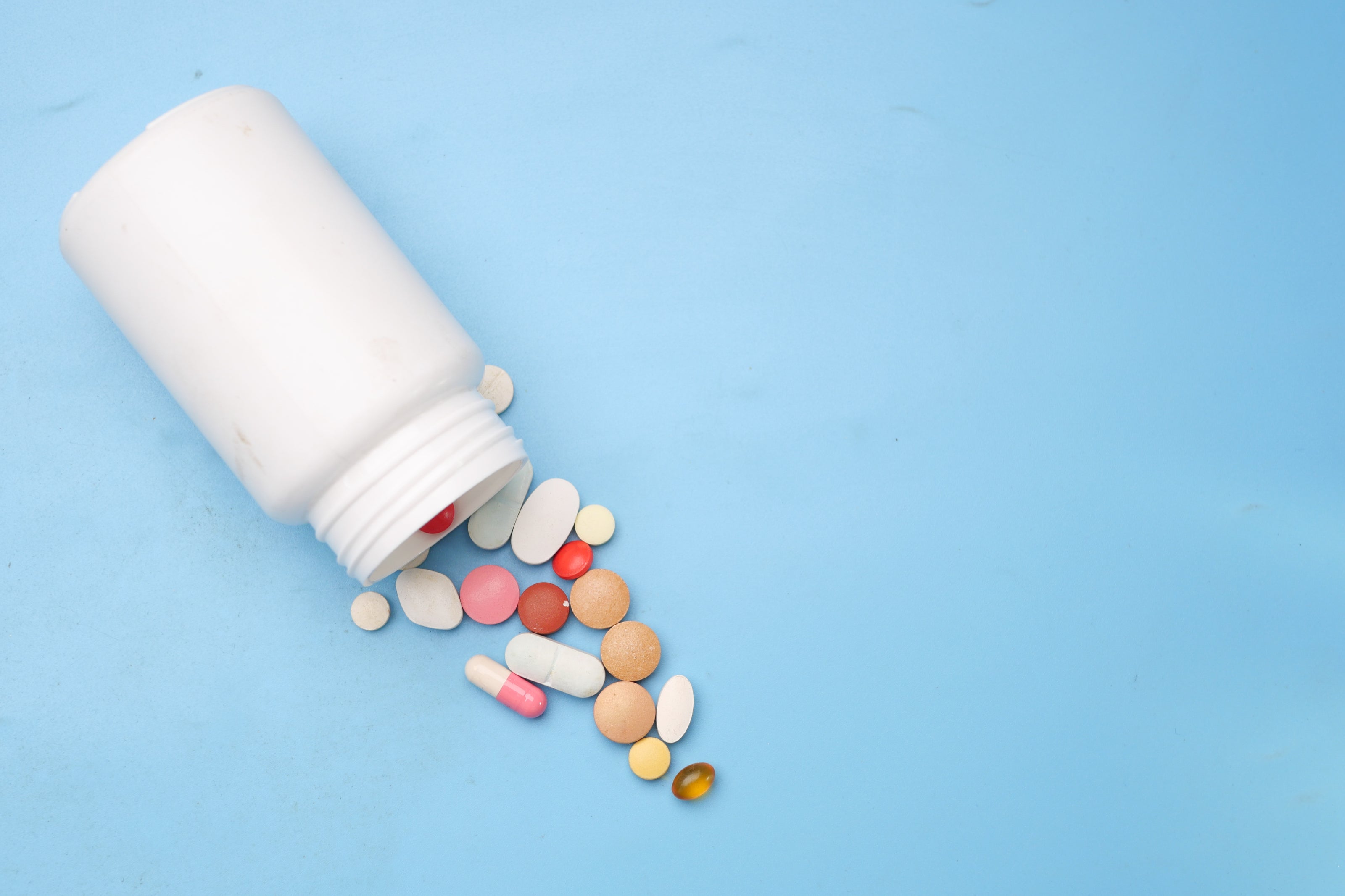 High-quality private label supplement manufacturing at Biowell Labs—assorted tablets and capsules spilling from a white bottle, representing premium contract supplement manufacturing in a Health Canada approved facility.