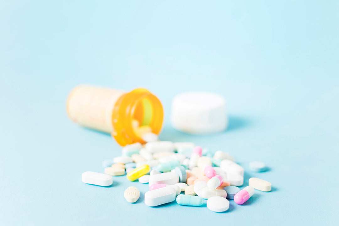 Nutraceutical tablets and capsules spilled from an open pill bottle onto a light blue background, representing high-quality nutraceutical manufacturing and supplement production at Biowell Labs.